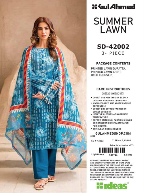 Woman wearing a blue printed outfit with a dupatta, standing against a beige wall with 'Gul Ahmed' branding.